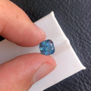 May include: A cushion-cut blue gemstone with a slightly darker blue center and a lighter blue edge.