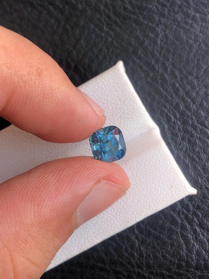May include: A cushion-cut blue gemstone with a slightly darker blue center and a lighter blue edge.