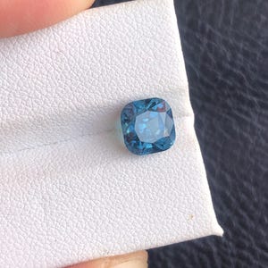 May include: A cushion-cut blue gemstone on a white background.