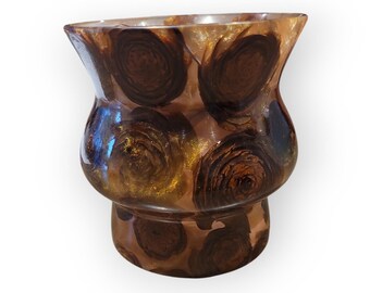 May include: A decorative vase with a unique design. The vase features a bulbous midsection and a flared top. The exterior is adorned with a pattern of dark brown, circular shapes against a translucent background with gold accents. The vase is made of a clear material.