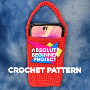 Peut inclure: Un étui de téléphone rouge crocheté avec une poignée, contenant un smartphone. Le texte "ABSOLUTE BEGINNER PROJECT CROCHET PATTERN" est en blanc. Le fond est un tissu bleu.