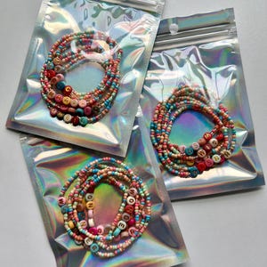 May include: Three clear plastic bags with zipper closures, each containing a colorful beaded bracelet with letter beads spelling out the words "MAGIC", "MISS", and "WONDER".