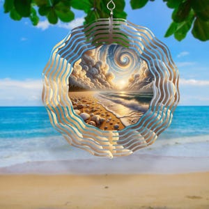 May include: A circular metal wind spinner featuring a wavy, layered frame design. The center displays a printed image of a sandy beach with seashells, a starfish, and ocean waves under a swirling, cloudy sky with a bright sun at the horizon.