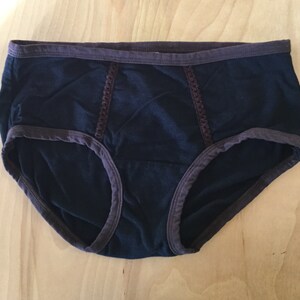 K&ouml;nnte beinhalten: Schwarze Unterw&auml;sche mit braunem Besatz und Spitzendetails.