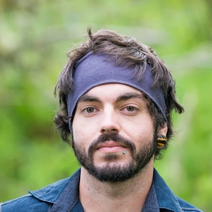 May include: A man with a dark blue headband, a dark beard, and a blue shirt. He is looking at the camera.