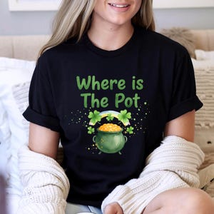 May include: Black t-shirt with the text "Where is The Pot" in green. The graphic includes a green pot of gold, a rainbow, and shamrocks, perfect for St. Patrick's Day.
