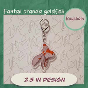 May include: A clear acrylic keychain featuring a Fantail Oranda goldfish design. The fish is white and orange, with a 2.5-inch design. The word "Keychain" is in a green circle. The text "Fantail oranda goldfish" is above the keychain.