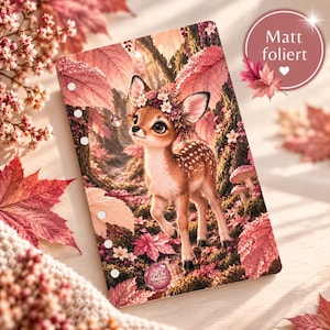 Könnte beinhalten: Eine rechteckige Planereinlage mit einem Reh mit Blumenkranz in einem Wald mit rosafarbenen und braunen Herbstblättern. Das Cover hat eine matte Oberfläche, sechs gelochte Ringlöcher an der linken Seite und ein kleines kreisförmiges Logo.
