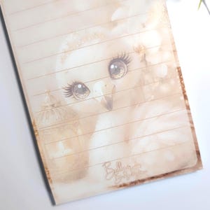 Op de afbeelding: Een gelijnd notitieblok met een sepia-getinte illustratie van een vogel met grote, gedetailleerde ogen. De vogel is het middelpunt, met een zachte, vage achtergrond. Het notitieblok heeft de tekst "Bella's Baby Store".