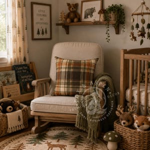 May include: A light beige upholstered rocking chair featuring a square plaid pillow in shades of orange, brown, and green. A textured olive green throw blanket with fringe hangs over the armrest, set in a room with woodland-themed decor.