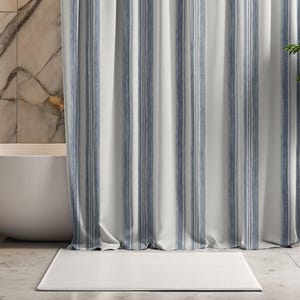May include: A white and blue striped shower curtain hangs in front of a white bathtub. A white rectangular bath mat sits on the floor in front of the curtain. The bathroom has a marble wall.