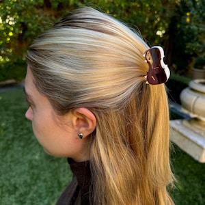 Può includere: Un fermaglio per capelli a forma di violino di colore marrone e oro con una finitura lucida.