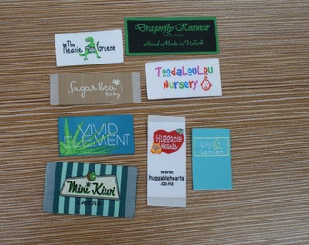 Puede incluir: Una colección de ocho etiquetas rectangulares de tela para ropa con varios nombres de marca y logotipos, incluyendo The Meanie Greene, Dragonfly Knitwear, Sugar bea baby, ToodaLouLou Nursery, VIVID ELEMENT, Huggable Hearts, Mini Kiwi y Lily & London.