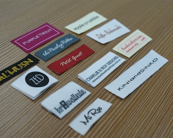 Puede incluir: Una colección de etiquetas rectangulares de tela para ropa en varios colores, incluyendo magenta, negro, rojo y blanco. Cada etiqueta presenta nombres de marca y logotipos únicos impresos en diferentes fuentes, como Purple Trout, Al'Husn, Zed, Petit Gosset y Kinianddinko.