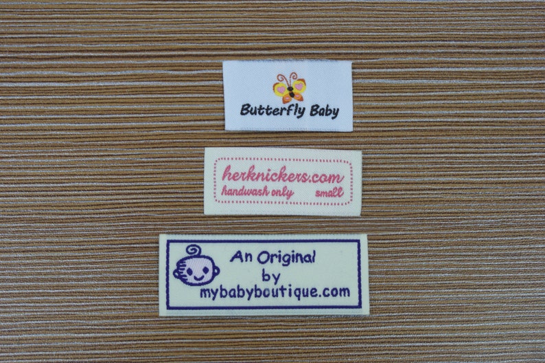 Puede incluir: Tres etiquetas rectangulares de tela con texto y gr&aacute;ficos. La etiqueta superior dice "Butterfly Baby" con un gr&aacute;fico de mariposa. La etiqueta del medio dice "herknickers.com handwash only small". La etiqueta inferior dice "An Original by mybabyboutique.com" con un beb&eacute;.