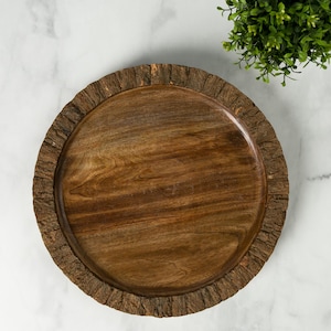 May include: A round, wooden serving tray with a natural bark edge. The tray is made of dark brown wood and has a smooth, polished surface. The bark edge adds a rustic touch to the tray. Perfect for serving appetizers or displaying decorative items.