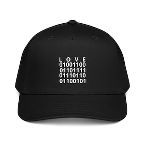 Może przedstawiać: Czarna czapka z daszkiem z napisem LOVE białymi wielkimi literami u góry, pod którym znajdują się cztery linie białego kodu binarnego. Czapka posiada usztywnianą koronę, zakrzywiony daszek oraz guzik na środku górnej części materiału.
