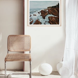 May include: A framed painting of a rocky coastline with crashing waves. The painting is in a light wood frame and is hanging on a white wall.