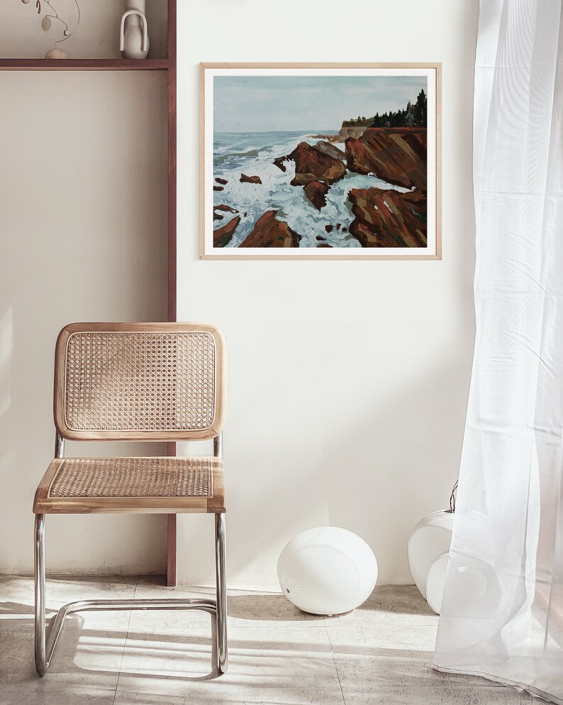 May include: A framed painting of a rocky coastline with crashing waves. The painting is in a light wood frame and is hanging on a white wall.