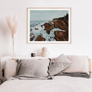 May include: A painting of a rocky coastline with crashing waves. The sky is a light blue and the water is a deep blue. The rocks are a reddish brown color. The painting is framed in a wooden frame.