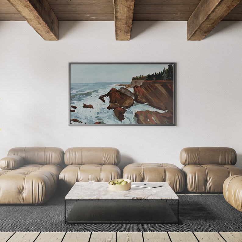 May include: A living room interior with a large framed painting of a seascape with rocky cliffs and crashing waves. The painting is hanging on a white wall above a brown leather sectional sofa. A coffee table with a marble top sits in front of the sofa.