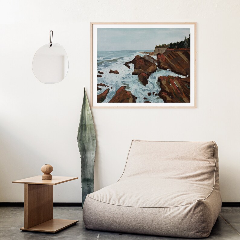 May include: A framed painting of a seascape with crashing waves and rocky cliffs. The painting is in a light wood frame and is hanging on a white wall.
