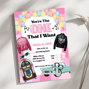 May include: A pink invitation with the text "You're The ONE That I Want" and "Millie is ONE." The design includes illustrations of a pink jacket, a black jacket, sunglasses, a jukebox, a milkshake, and a light blue car. The invitation also includes event details.