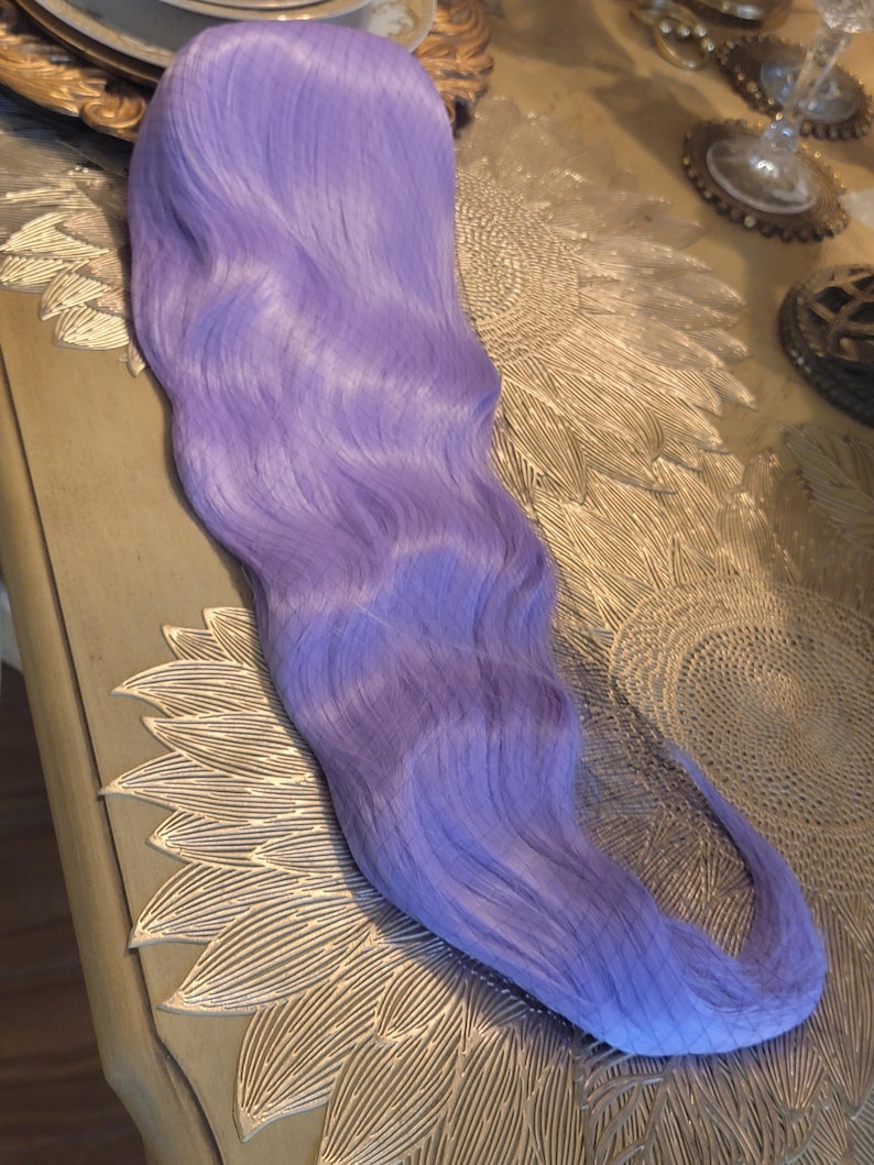Puede incluir: Una peluca larga y ondulada de un vibrante color morado lavanda. Las fibras capilares son lisas y est&aacute;n peinadas con ondas suaves y fluidas que se extienden desde la coronilla hasta las puntas, creando una textura uniforme en toda la longitud.