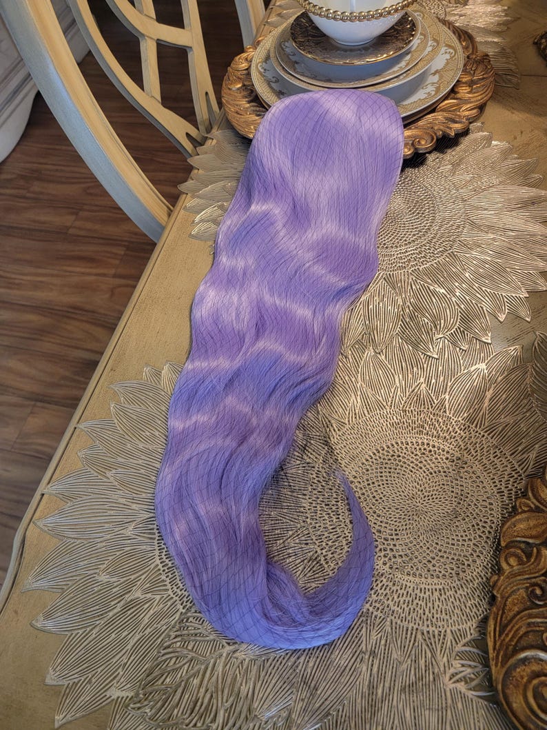 Puede incluir: Una extensi&oacute;n de cabello sint&eacute;tico largo y ondulado en un vibrante color morado lavanda. La pieza de cabello presenta una textura suave y fluida con ondas suaves a lo largo de toda su extensi&oacute;n, mostrando un tono morado claro uniforme.