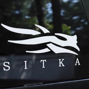 May include: White decal featuring a stylized design and the word "SITKA" in a serif font. The design is a series of curved lines and shapes, resembling a bird or abstract creature. The decal is on a black surface.
