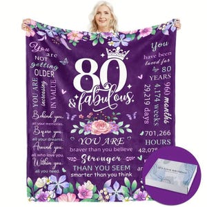 May include: Purple fleece blanket with a floral design and the number 80 in white with the words "& fabulous" below it. The text "You are not getting older, you are increasing in value" is on the left side of the blanket. The text "You have been loved for 80 years" is on the right side of the blanket. The blanket also includes a list of time measurements in years, weeks, months, days, hours, and minutes.