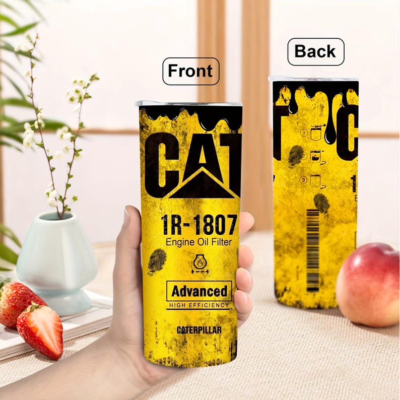 Op de afbeelding: Een gele en zwarte CAT-branded tumbler met het CAT-logo en de tekst "1R-1807 Engine Oil Filter". De tumbler heeft een distressed design en de woorden "Advanced High Efficiency" en "Caterpillar" staan ook op de voorkant.