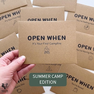 May include: Kraft paper cards with the words "OPEN WHEN" printed in black. One card reads "It's Your First Campfire" with a campfire graphic. The cards are part of the "Summer Camp Edition" collection.