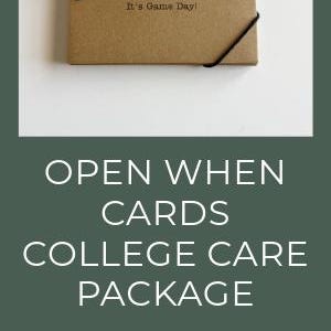May include: Kraft paper "Open When" cards with black script and a heart design. The cards are part of a college care package. The image also shows a black pen and a gift card.