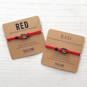 May include: Two red cord bracelets with black metal links, each mounted on a tan card. The cards feature the text RED Remember Everyone Deployed, Valor Craftworks, and phrases about support, solidarity, and waiting for those who serve far from home.