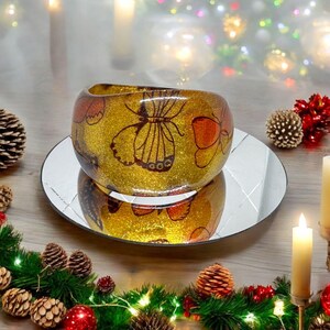 May include: A gold glitter resin bangle bracelet featuring a butterfly design. The bracelet is decorated with multiple butterflies in shades of orange, brown, and black.