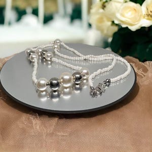 May include: A white pearl necklace with silver beads. The necklace is layered and has a silver clasp.