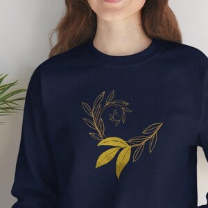 May include: A navy blue sweatshirt featuring a gold leaf design. The design is a spiral of leaves, creating a unique and modern look.