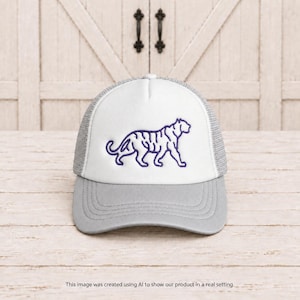 May include: A trucker hat featuring a white front panel with a dark purple embroidered tiger outline. The hat has a light gray brim and matching light gray mesh side and back panels. The design is centered on the front panel of the cap.
