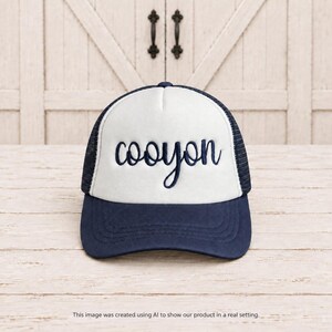 May include: A navy blue and white trucker hat featuring a foam front panel with the word cooyon embroidered in navy blue script lettering. The cap includes a solid navy blue brim and a mesh back panel, designed with a structured crown and adjustable strap.