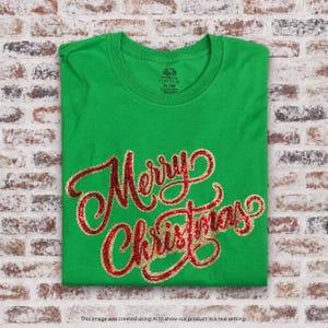 Op de afbeelding: Een felgroen T-shirt met korte mouwen en de tekst Merry Christmas in rode en gouden glitterende cursieve letters op de borst. Het shirt heeft een ronde hals en een Fruit of the Loom Platinum label geprint in de binnenkant van de kraag.