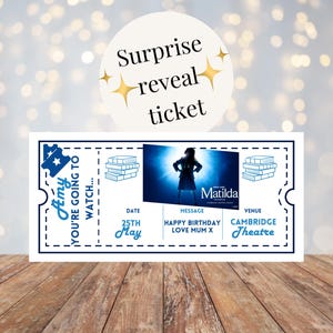Könnte beinhalten: Ein weißes Ticket mit blauem Text und einem Bild aus dem Musical "Matilda". Auf dem Ticket steht "Amy, du wirst..." und enthält das Datum "25. Mai", eine Nachricht und den Veranstaltungsort "Cambridge Theatre".