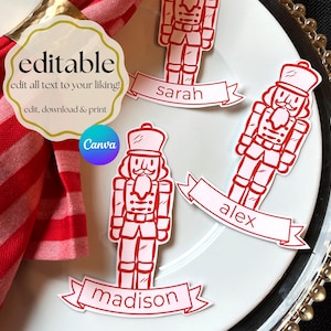 Op de afbeelding: Rode en witte notenkraker-naamkaartjes met namen op banners, gerangschikt op een wit bord met een gouden kralenrand. De woorden "editable" en "Canva" zijn ook zichtbaar.