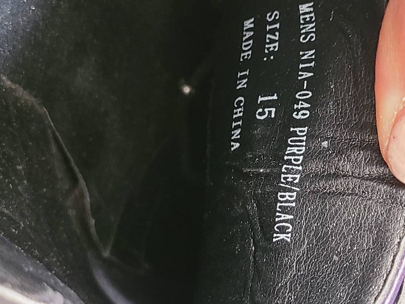 May include: Close-up of the inside of a shoe showing the size, color, and manufacturer information. The text reads "Mens NIA-049 Purple/Black Size: 15 Made in China."