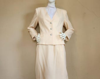 May include: A cream-colored suit jacket and skirt set. The jacket has a V-neck and a button closure. The skirt is knee-length and has a straight silhouette.