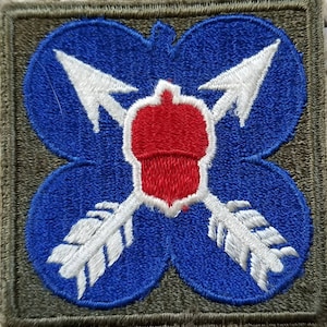 May include: A blue and white embroidered patch with a red acorn in the center. Two white arrows with feathers cross behind the acorn. The patch is surrounded by a green border.