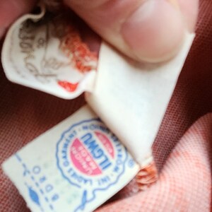 May include: Close-up of a white label with blue text and a red circle. The text reads "ILGWU, Made in USA, Union Label".