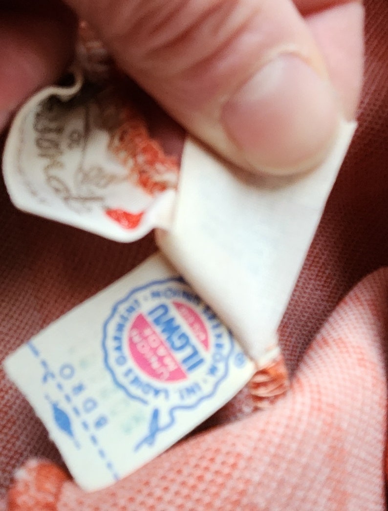 May include: Close-up of a white label with blue text and a red circle. The text reads "ILGWU, Made in USA, Union Label".