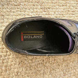 May include: Close-up of the inside of a black leather dress shoe with a purple and black ombre design. The shoe has a black leather insole with the word "BOLANO" printed on it.