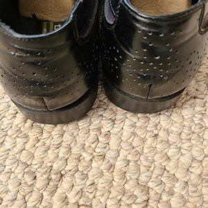 May include: A pair of black leather shoes with a perforated design. The shoes have a rounded toe and a low heel.